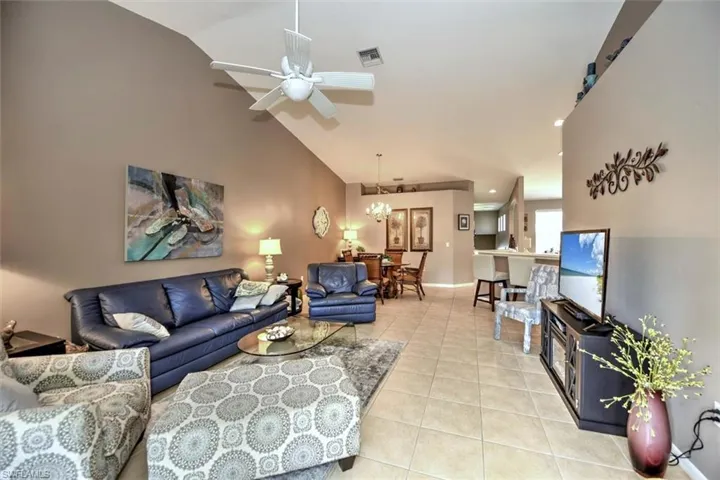 Living area with visible vents, baseboards, ceiling fan, light tile patterned flooring, and lofted ceiling
