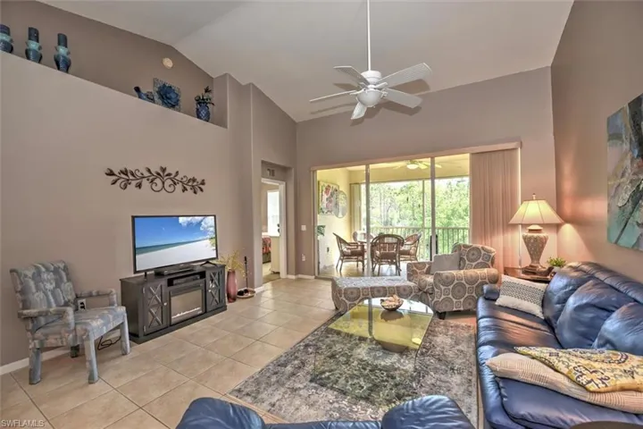 Living area featuring high vaulted ceiling, light tile patterned floors, baseboards, and a ceiling fan