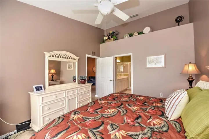 Carpeted bedroom featuring a high ceiling, ensuite bathroom, ceiling fan, and visible vents