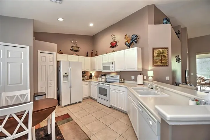 Kitchen with white appliances, white cabinets, light tile patterned flooring, light countertops, and a sink