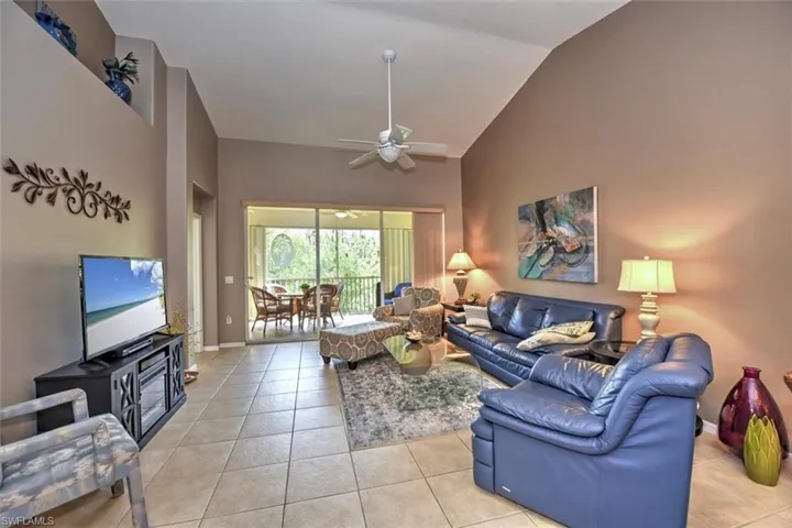 Living area featuring high vaulted ceiling, light tile patterned floors, baseboards, and a ceiling fan