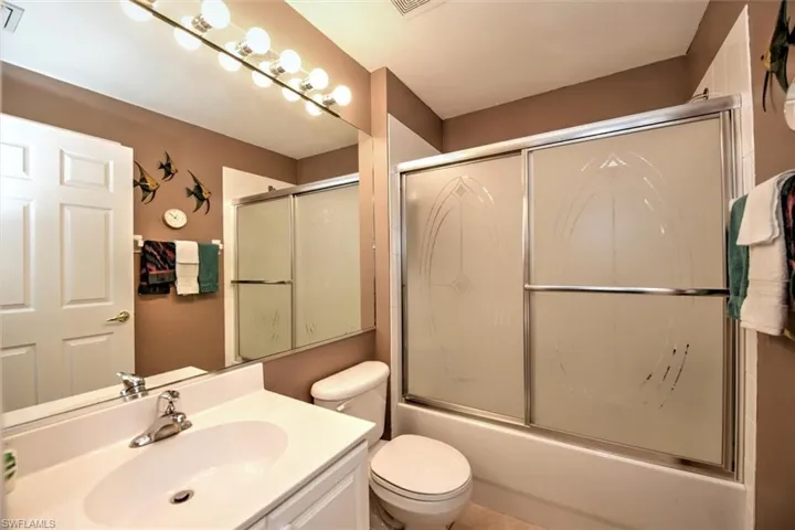 Bathroom with toilet, shower / bath combination with glass door, vanity, and visible vents