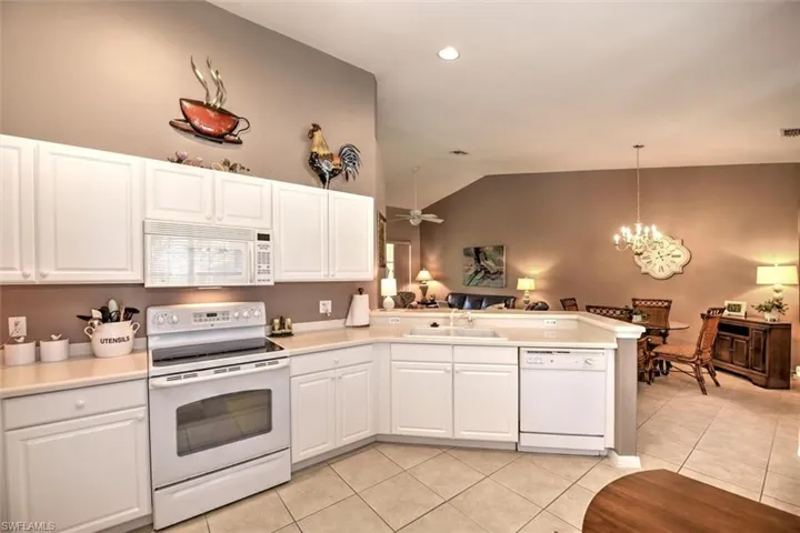 Kitchen with white appliances, a peninsula, vaulted ceiling, light tile patterned flooring, and a sink