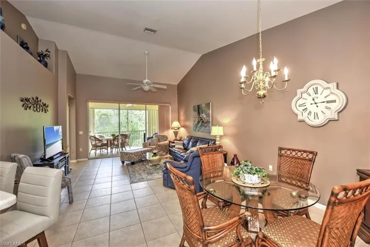 Dining space featuring visible vents, baseboards, light tile patterned floors, ceiling fan with notable chandelier, and high vaulted ceiling