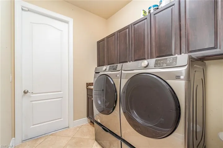 Clothes washing area featuring washer and dryer, cabinets, and light tile patterned floors