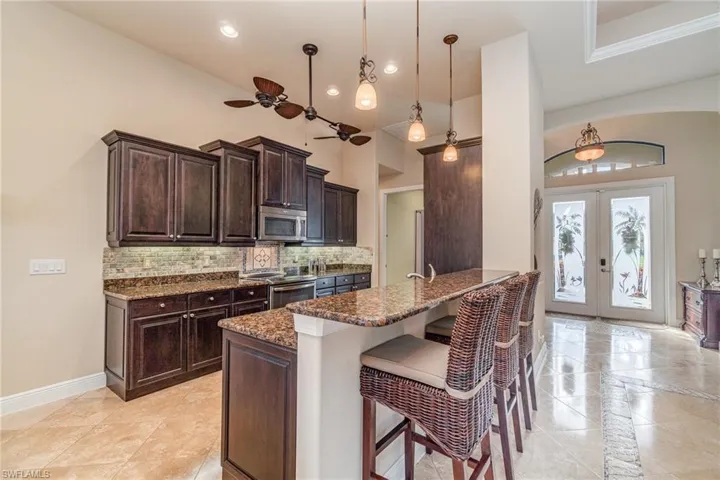 Kitchen with french doors, a kitchen breakfast bar, a towering ceiling, pendant lighting, and appliances with stainless steel finishes