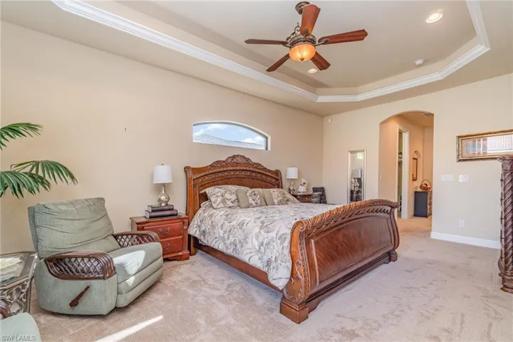 Bedroom with light colored carpet, crown molding, ceiling fan, and a tray ceiling