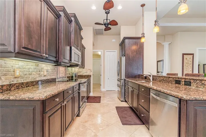 Kitchen featuring appliances with stainless steel finishes, ornate columns, dark brown cabinets, sink, and decorative light fixtures