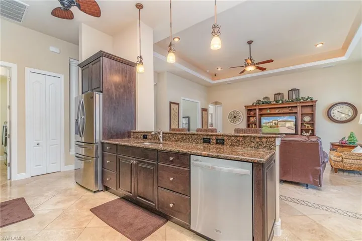 Kitchen with hanging light fixtures, appliances with stainless steel finishes, a tray ceiling, and dark brown cabinets