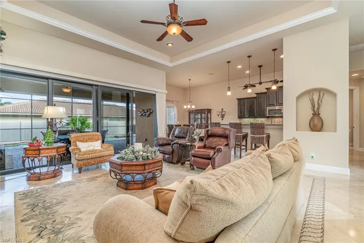 Living room with a raised ceiling, plenty of natural light, and ceiling fan with notable chandelier