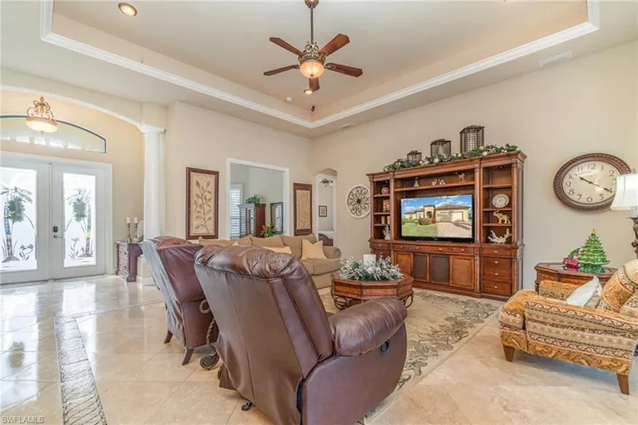 Living room with ceiling fan, ornate columns, a tray ceiling, and french doors
