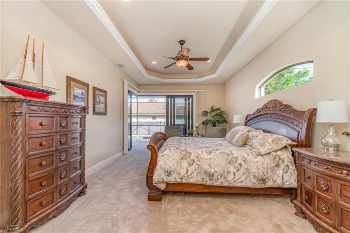 Carpeted bedroom featuring a tray ceiling, access to exterior, and ceiling fan