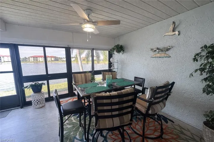 Sunroom / solarium featuring a textured wall, a water view, wood ceiling, a ceiling fan, and outdoor dining space