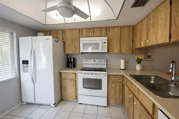 Kitchen with white appliances, light countertops, light tile patterned floors, a ceiling fan, and brown cabinetry