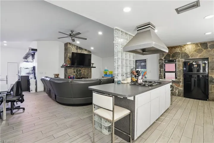 Kitchen featuring dark countertops, white cabinetry, a kitchen breakfast bar, island range hood, and lofted ceiling