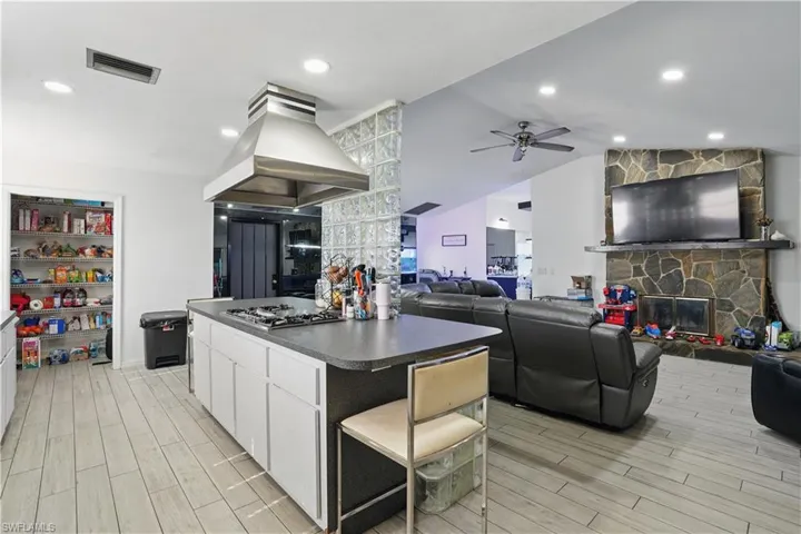Kitchen featuring dark countertops, white cabinetry, island range hood, open floor plan, and wood finish floors