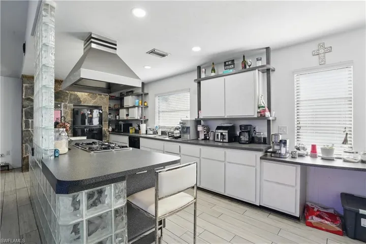 Kitchen featuring a kitchen bar, island range hood, wood finish floors, dark countertops, and recessed lighting