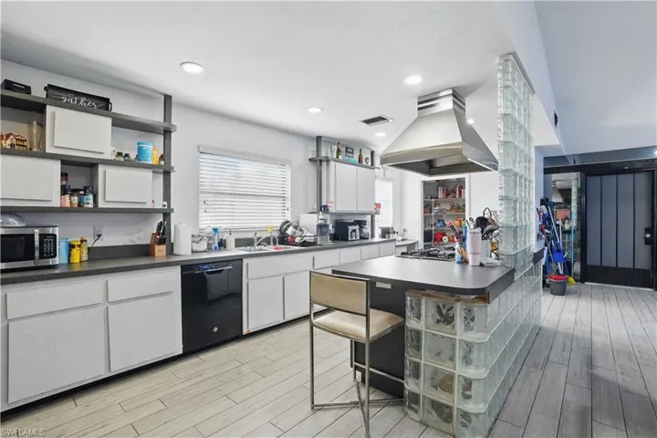Kitchen with dark countertops, a kitchen breakfast bar, light wood-style floors, island exhaust hood, and recessed lighting