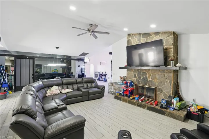 Living area with a stone fireplace, vaulted ceiling, wood finished floors, ceiling fan, and recessed lighting