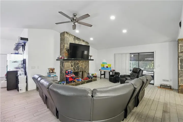 Living room featuring lofted ceiling, a fireplace, light wood-type flooring, ceiling fan, and recessed lighting