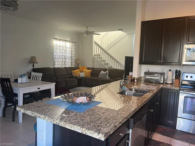 Kitchen featuring light stone counters, stainless steel appliances, light tile patterned floors, open floor plan, and ceiling fan