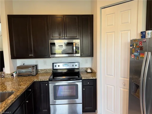 Kitchen featuring stainless steel appliances, dark brown cabinets, and dark stone counters