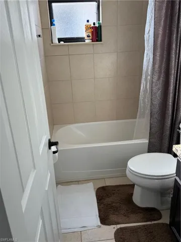 Bathroom with light tile patterned floors, shower / bath combo with shower curtain, and vanity