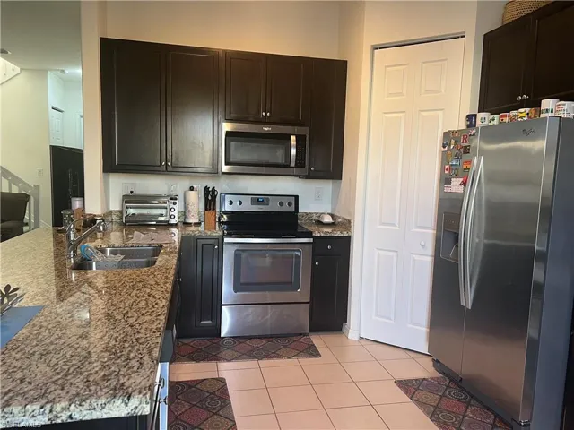 Kitchen featuring stainless steel appliances, light stone countertops, light tile patterned floors, a peninsula, and dark brown cabinetry