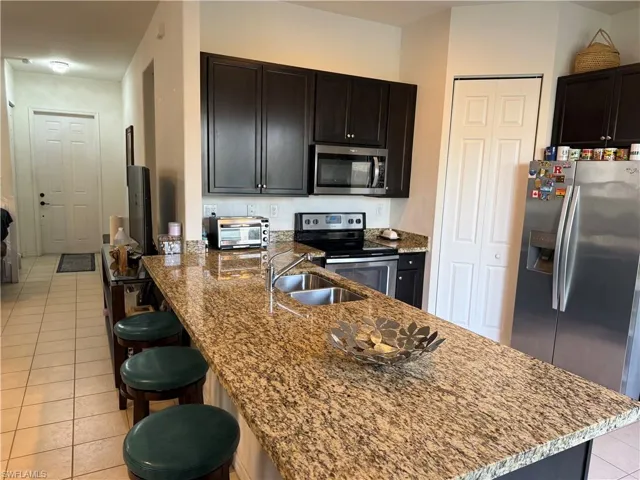 Kitchen with a peninsula, light tile patterned floors, a breakfast bar area, appliances with stainless steel finishes, and dark stone counters