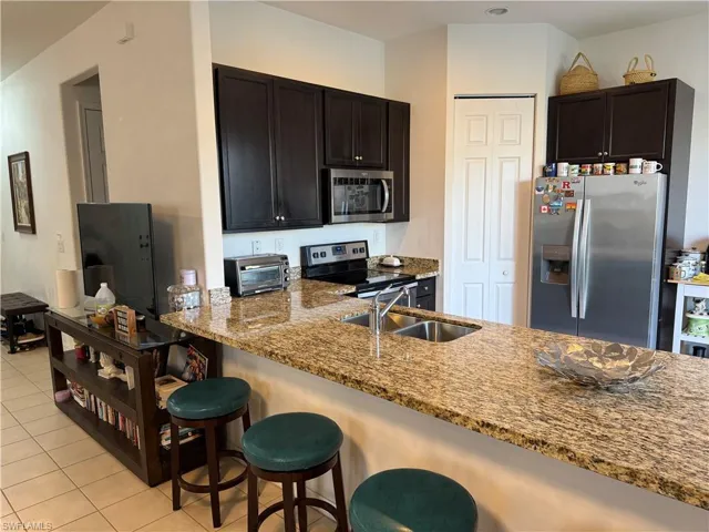 Kitchen featuring a kitchen bar, stainless steel appliances, a peninsula, light stone countertops, and light tile patterned floors