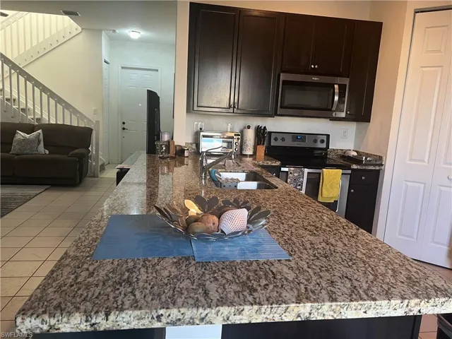 Kitchen featuring dark stone counters, appliances with stainless steel finishes, light tile patterned floors, open floor plan, and dark brown cabinetry