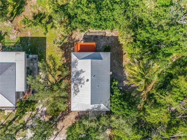 Aerial perspective of residential property featuring a metal roof, rear wooden deck, and surrounding dense mature trees