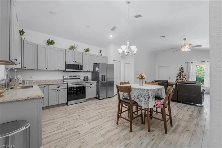 Kitchen with stainless steel appliances, hanging lights, gray cabinets, light stone countertops, and light wood-type flooring