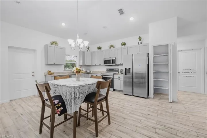 Kitchen featuring gray cabinetry, stainless steel appliances, light wood-style floors, hanging lights, and light stone countertops