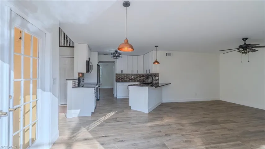 Kitchen with white cabinets, backsplash, ceiling fan, decorative light fixtures, and a peninsula