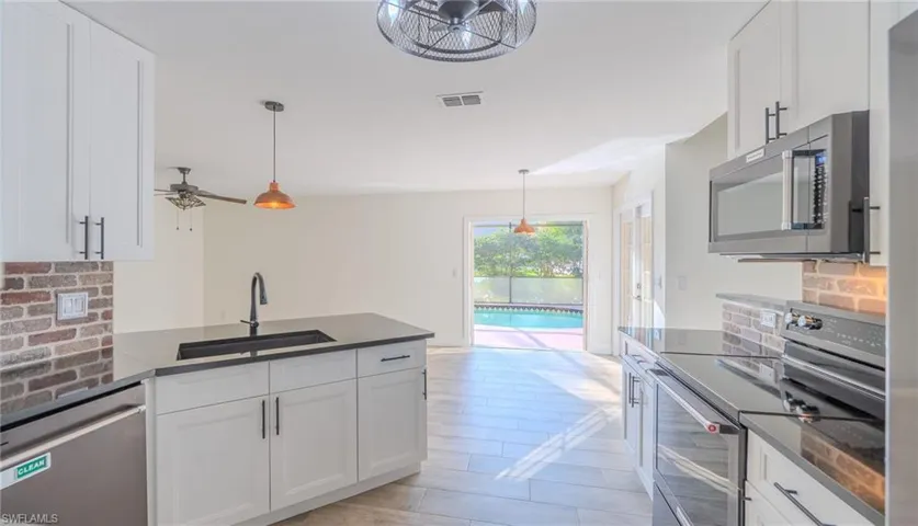 Kitchen featuring stainless steel appliances, white cabinetry, decorative backsplash, a peninsula, and ceiling fan