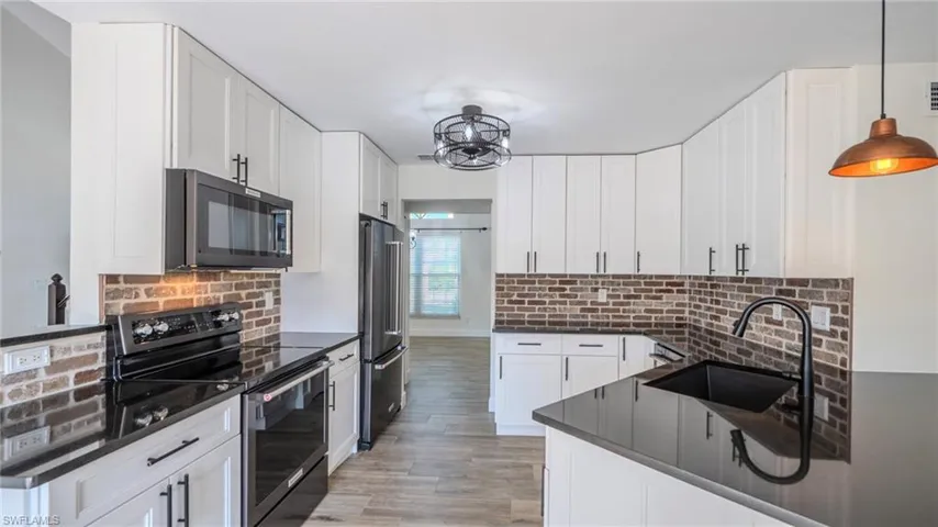 Kitchen with stainless steel appliances, white cabinetry, dark stone counters, and light wood-type flooring