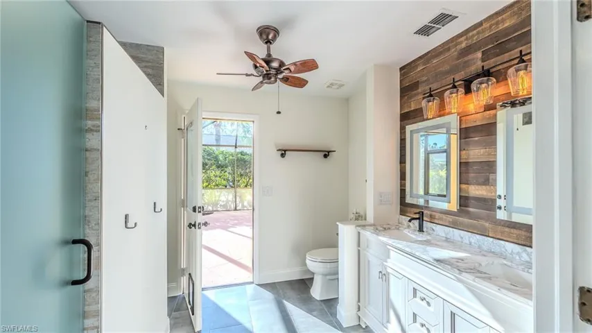 Bathroom with double vanity, wood walls, a ceiling fan, and a shower stall