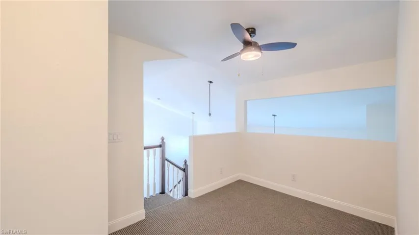 Spare room with dark colored carpet, ceiling fan, and vaulted ceiling