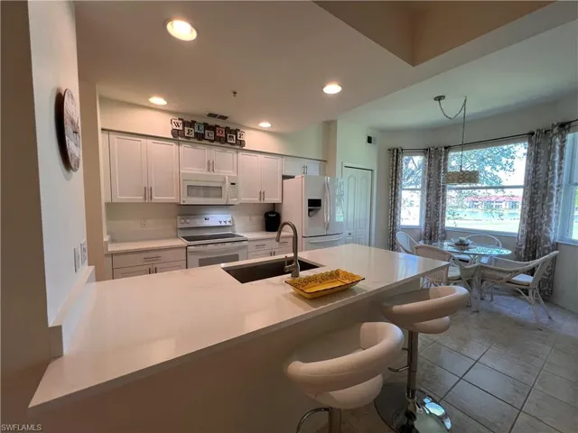 Kitchen with white Shaker cabinetry, sink, a kitchen breakfast bar, pendant lighting, and white appliances