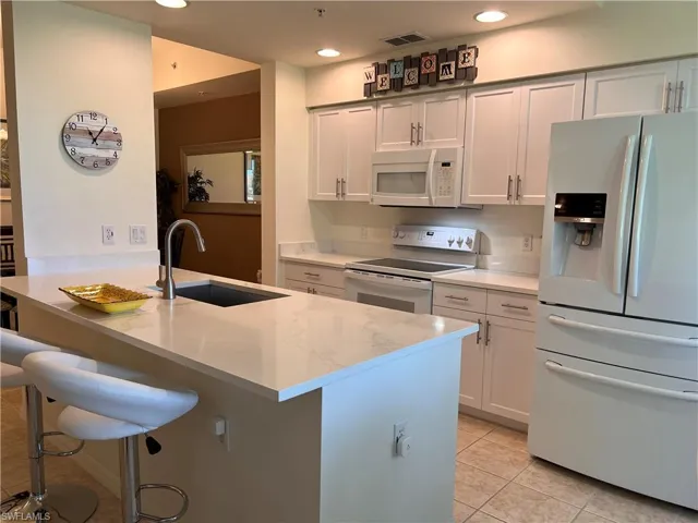 Kitchen with light stone countertops, white appliances, sink, light tile patterned floors, and white cabinetry