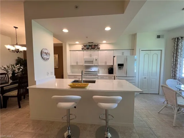 Kitchen with white cabinetry, sink, stainless steel appliances, an inviting chandelier, and a kitchen bar
