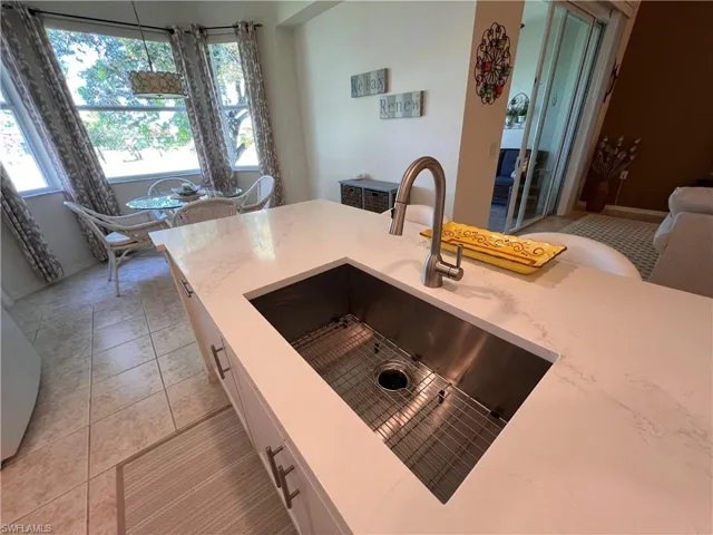 Kitchen with light quartz countertops, white cabinetry, sink, hanging light fixtures, and light tile patterned floors