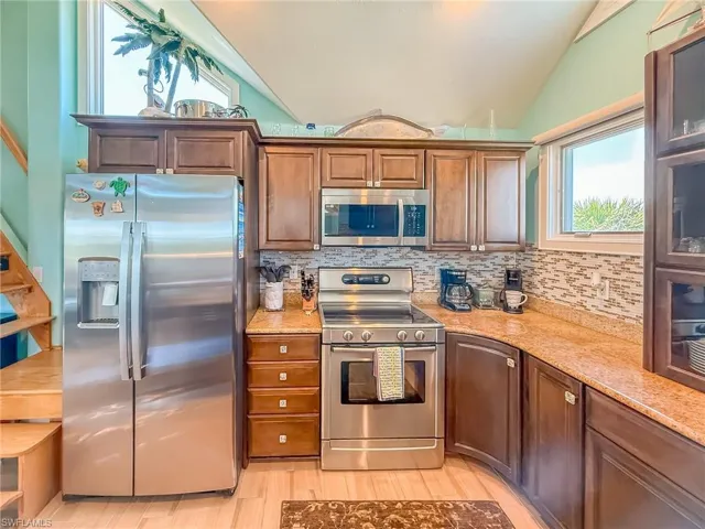 Kitchen featuring light wood-style flooring, appliances with stainless steel finishes, brown cabinets, vaulted ceiling, and backsplash