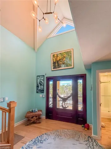 Entryway with high vaulted ceiling, a healthy amount of sunlight, wood finished floors, and a notable chandelier