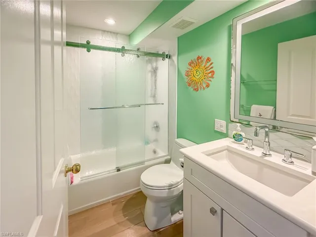 Bathroom with visible vents, toilet, shower / bath combination with glass door, wood finished floors, and vanity