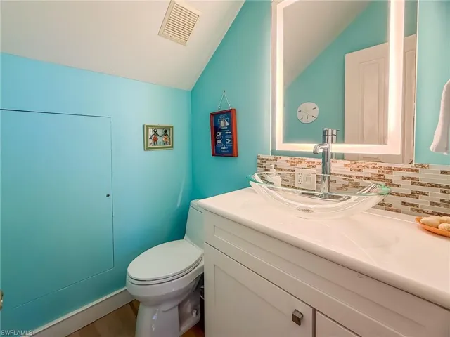 Half bathroom featuring tasteful backsplash, visible vents, vaulted ceiling, and vanity