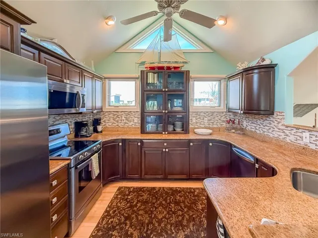 Kitchen with dark brown cabinetry, appliances with stainless steel finishes, and vaulted ceiling