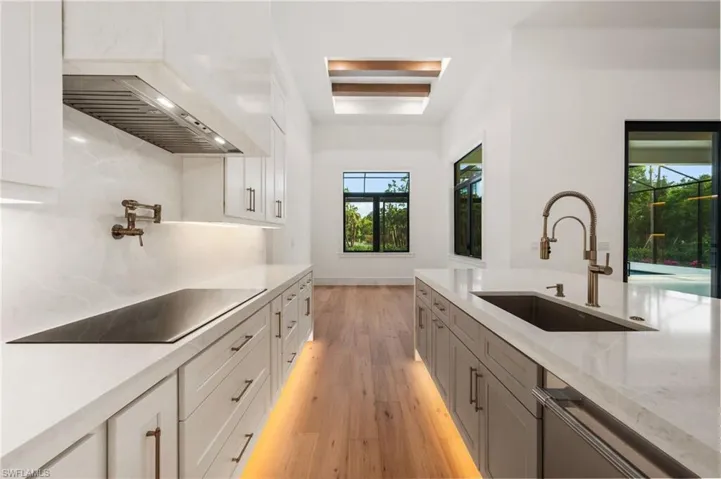 Kitchen featuring light stone counters, white cabinets, decorative backsplash, light wood finished floors, and a sink