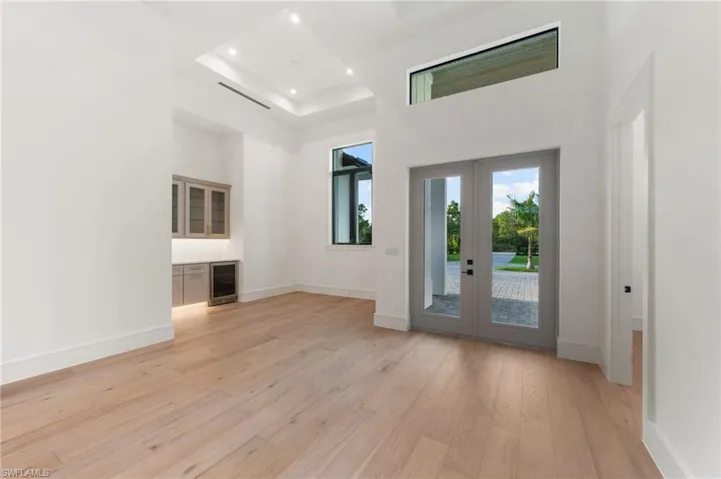 Foyer featuring light wood-type flooring, a high ceiling, beverage cooler, french doors, and baseboards